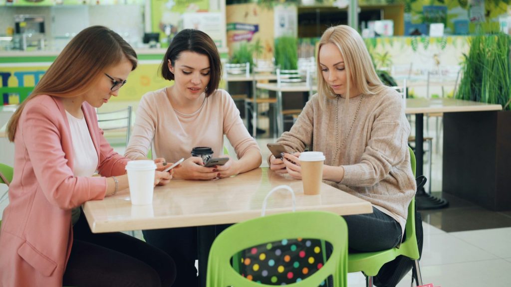 Trois femmes regardant leurs téléphones à une table de café.
